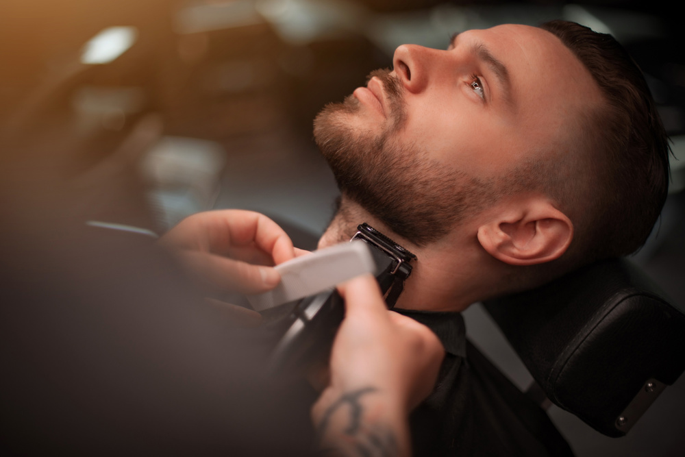 Close-up of a man receiving a precise neck and beard trim with electric clippers at a modern barbershop, showing careful grooming and relaxation in a professional setting