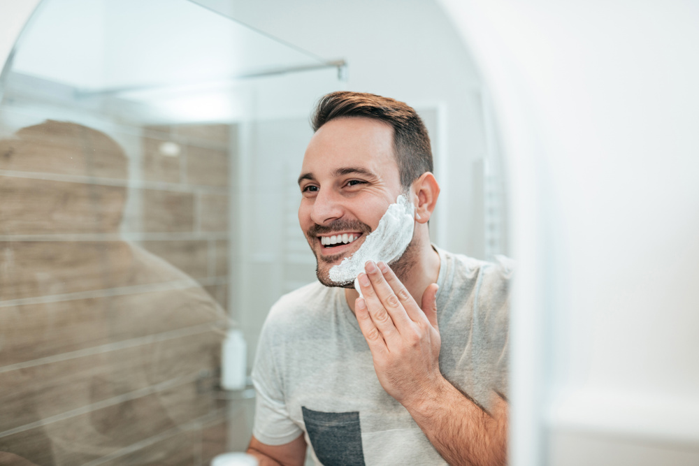 Handsome man applying shaving cream, reflection in the mirror image