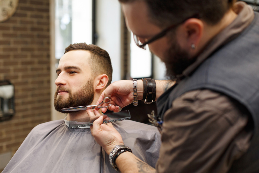 Barber styling beard with scissors at barbershop