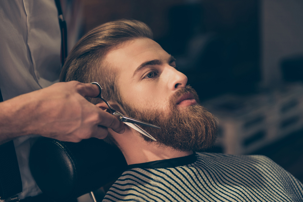 Close up of a hairdresser`s work for a young man’s beard at the barber shop