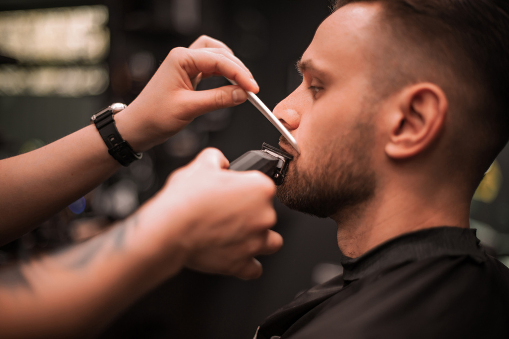 Close-up of a barber trimming a client's mustache with electric clippers and a comb