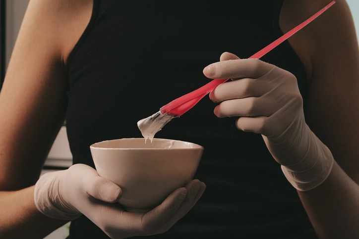 Girl in white rubber protective gloves holding a brush in her hands and stirring hair dye close-up colorist hair care at home hair mask