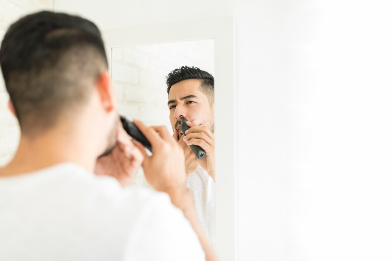 Reflection of man cutting his nasal hair with trimmer in bathroom